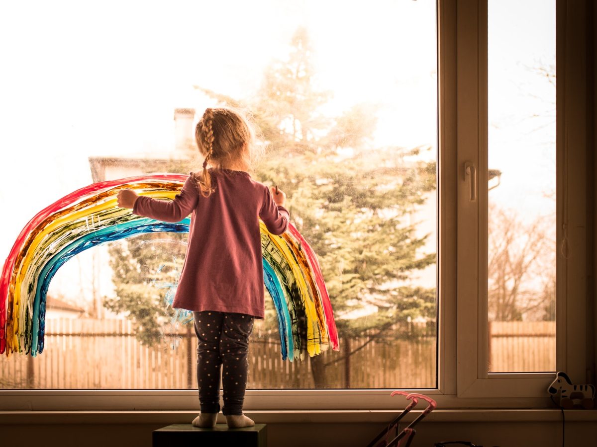 Little girl painting colorful, vibrant rainbow on window